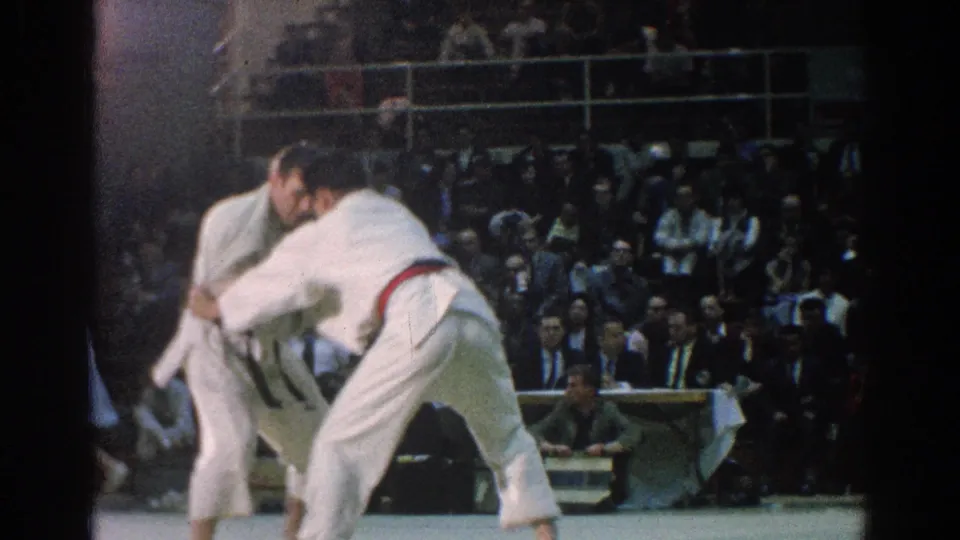During the San Gabriel judo match, the red-belt competitor leans into a throw attempt as the opponent holds position.