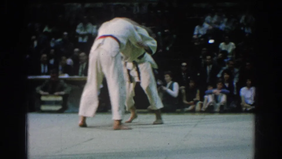 Near the end of the clip, one competitor bends over the other in a judo throw or balance struggle on the San Gabriel arena mat.