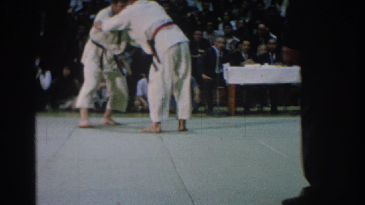 Two men in white gi spar on a mat as a referee stands close by.
