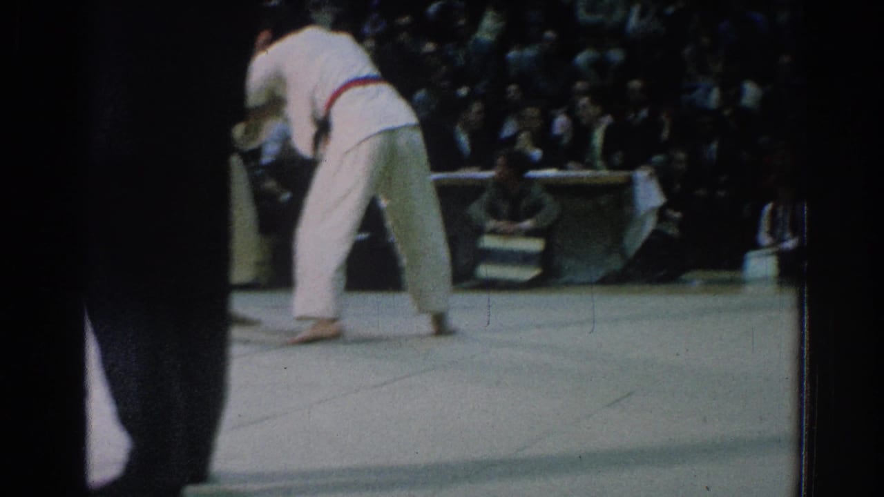 A 1966 San Gabriel karate bout continues as two gi-clad competitors move across the mat before judges and spectators.