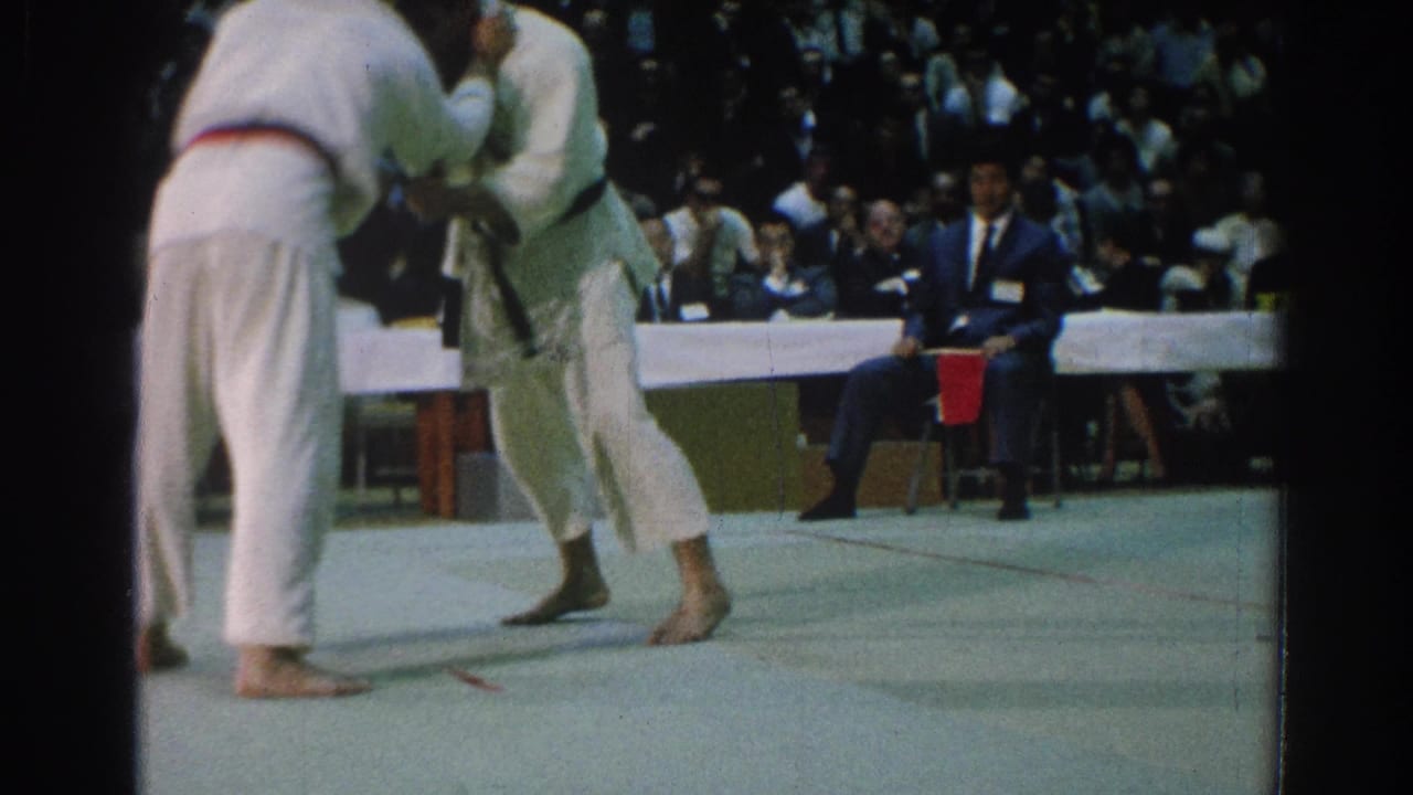 A 1966 San Gabriel martial arts match shows two men in white gi locked in a standing grapple before judges and spectators.