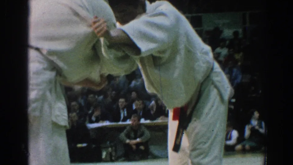 A closer 1966 San Gabriel frame shows a black-belt competitor gripping an opponent's sleeve during the martial arts match.