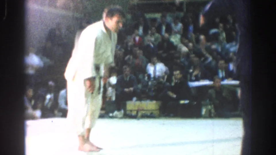 Two competitors in gi uniforms stand on an indoor mat before spectators during the San Gabriel martial arts competition.
