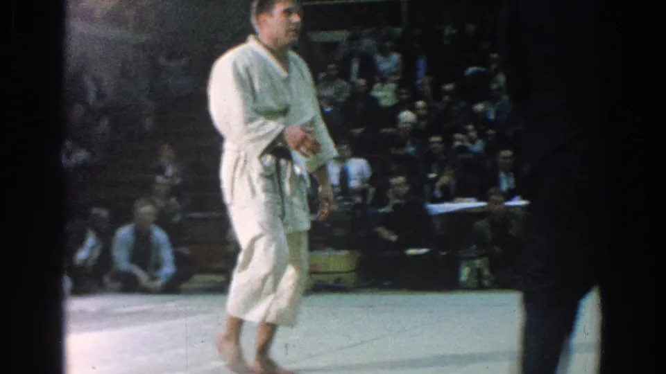 1966 San Gabriel karate tournament frame showing a white-gi competitor on the mat with spectators behind him.