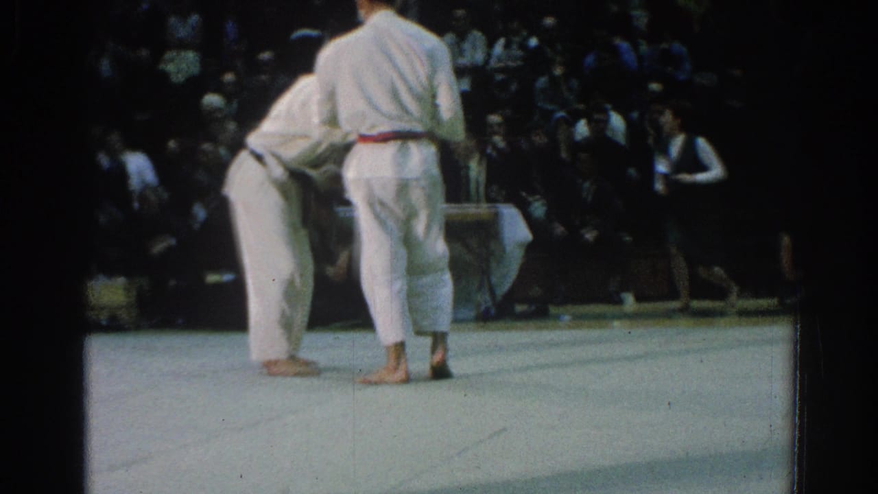 Two competitors in white gi face off on the mat during the San Gabriel karate tournament, with a referee nearby.