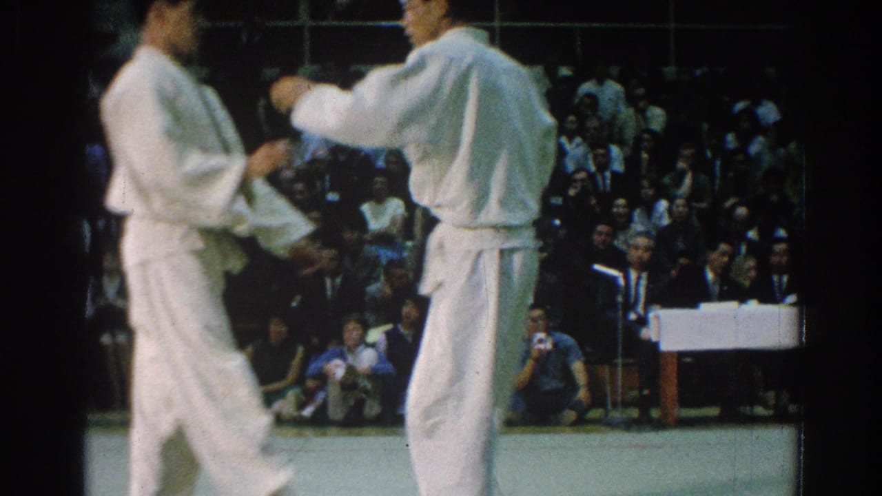 Two male karate competitors reset or circle on the mat during the 1966 San Gabriel indoor tournament footage.