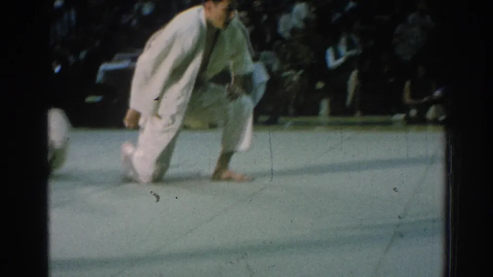 The home-movie frame shows two judo competitors in white gi moving low on the mat, partly blurred by motion and handheld filming.