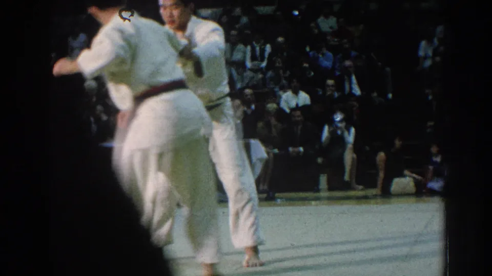 A 1966 San Gabriel tournament moment shows two white-uniformed martial artists in close contact on the mat before an audience.