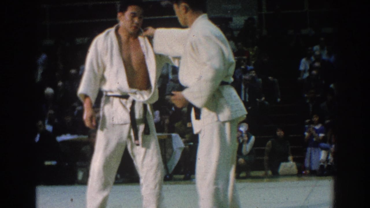 One judo athlete adjusts another athlete's gi while they stand on the mat.