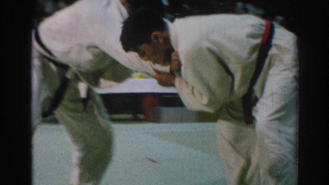 Two judo competitors bend forward and grip each other on an indoor mat.