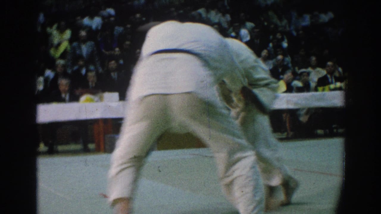A judo competitor bends low while holding an opponent on the mat.