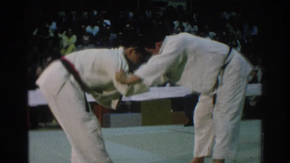 Two barefoot judo competitors lean into a standing grip exchange on an indoor mat in 1966 San Gabriel footage.