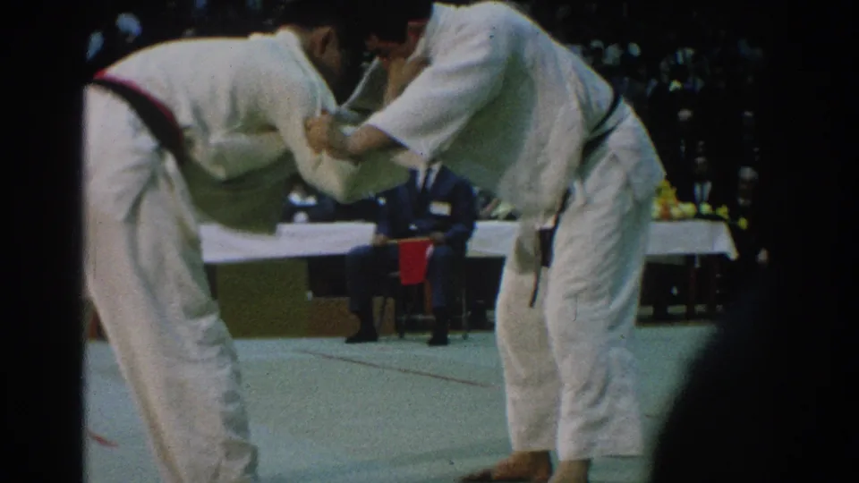 The San Gabriel judo match shows two competitors gripping each other with officials and spectators visible behind them.