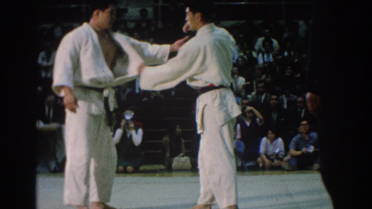 San Gabriel 1966 judo competitors in white gi stand on the mat as one reaches toward the other's uniform.