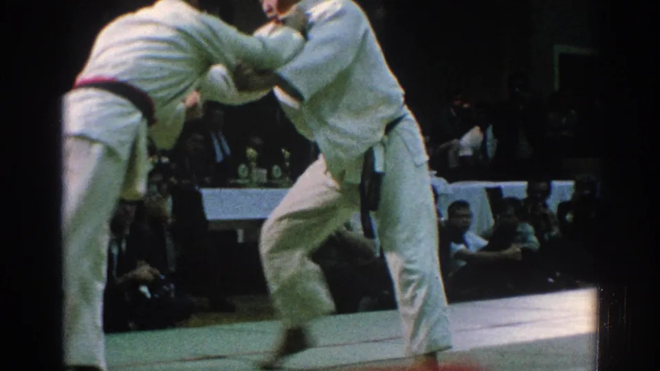 Near the end of the clip, two white-gi competitors remain locked in a standing grapple before a seated audience in the 1966 San Gabriel scene.