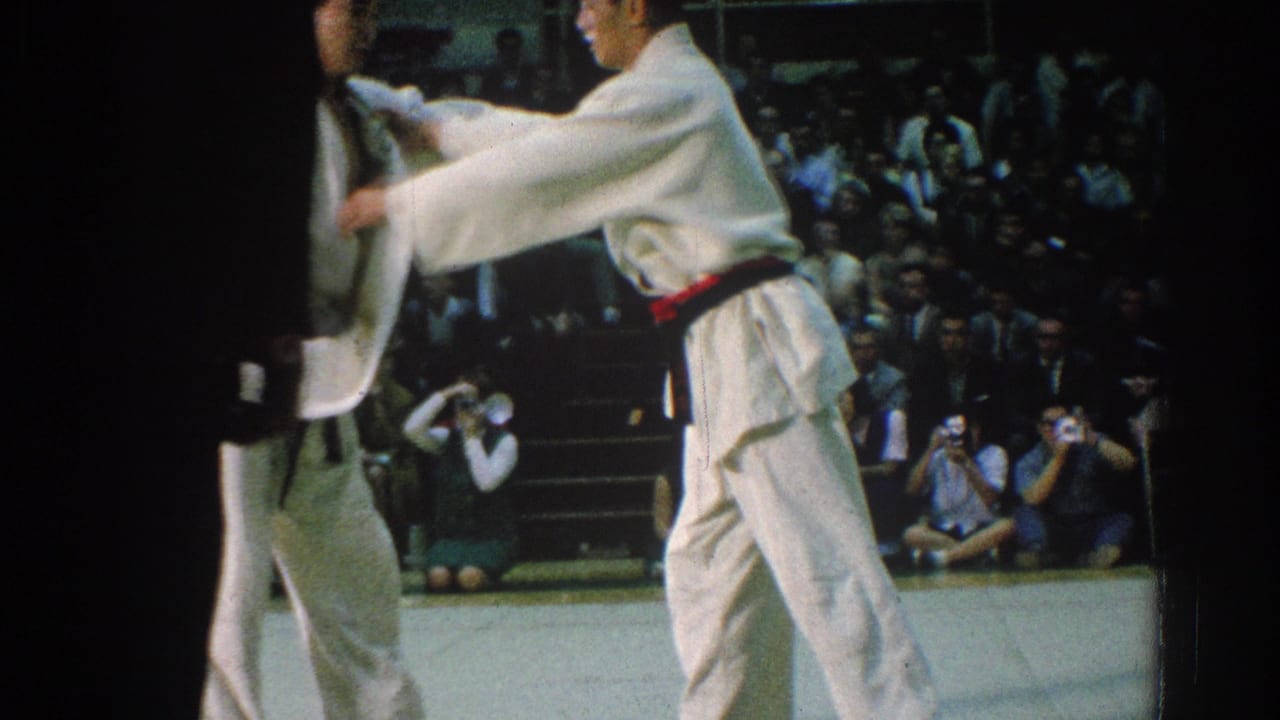 A judoka grips another competitor near the edge of the mat while spectators watch.