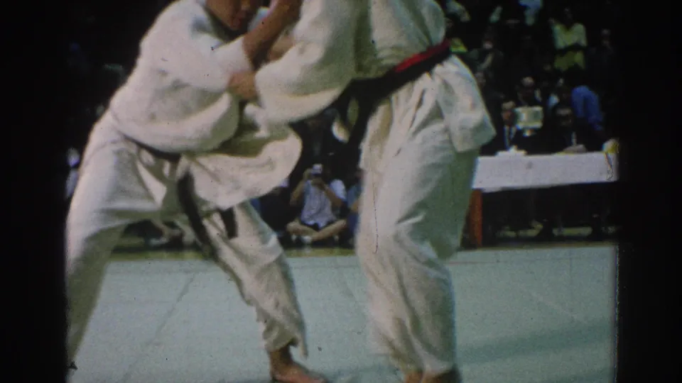 During the 1966 San Gabriel judo competition, one competitor is pulled forward in a throw attempt while spectators sit beyond the mat.