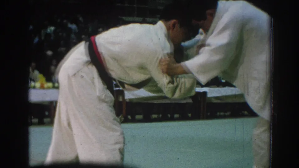 A close view of the 1966 judo bout shows one athlete bent forward while his opponent controls the gi near the mat edge.