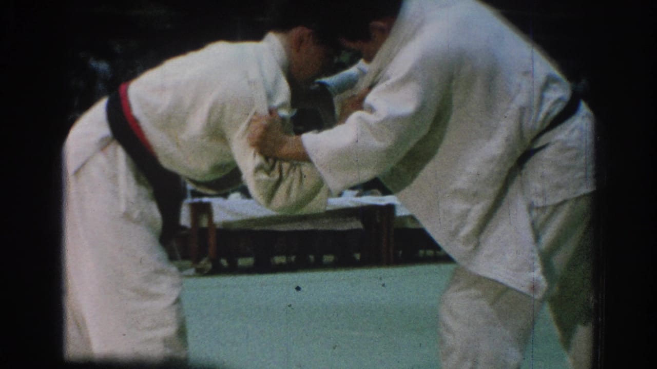 San Gabriel 1966 home-movie frame of two men in white gi gripping at close range during an indoor martial arts bout.
