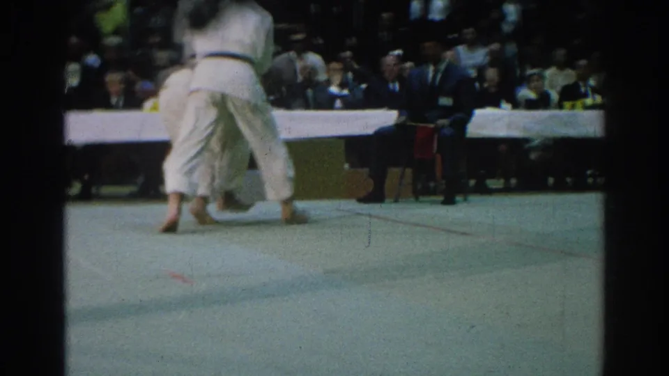 Wide 1966 San Gabriel tournament view showing two men in white gi moving on the mat with spectators and officials behind them.