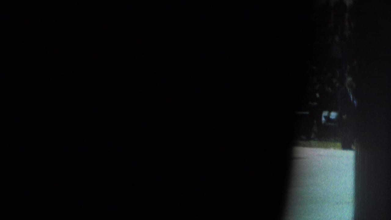 Obscured 1966 8mm frame from San Gabriel footage, showing mostly darkness with a narrow bright opening and indistinct outdoor or entryway detail.