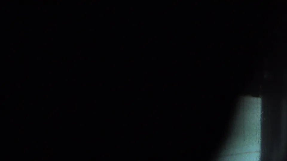 Obscured 8mm frame with heavy shadow and a small pale vertical strip, likely from the camera being blocked or turned before the indoor scene.