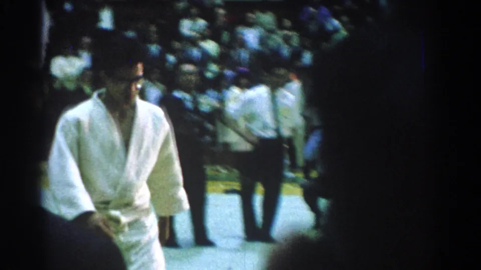 1966 San Gabriel home-movie frame showing a martial arts competitor in a white gi moving across the competition floor.