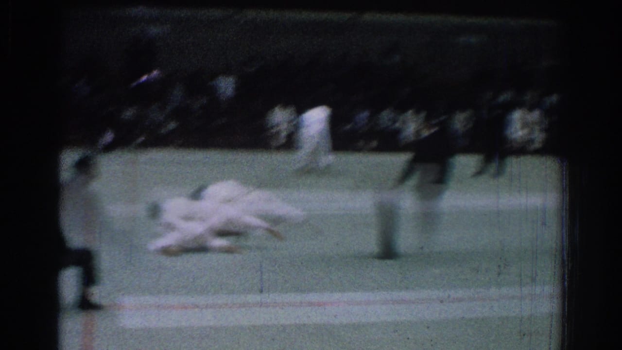 Two judo competitors are blurred in motion on the mat with a referee and spectators nearby.