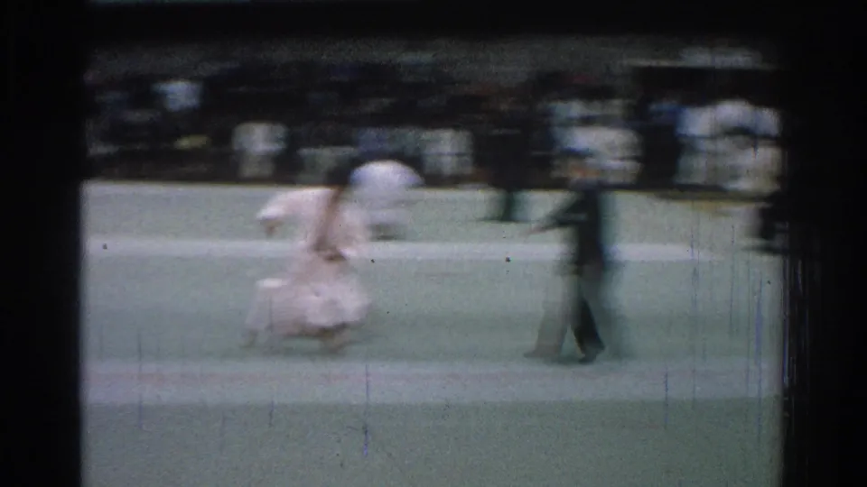 During the 1966 San Gabriel judo match, one competitor leans over another on the green mat while a figure passes in front of the camera.