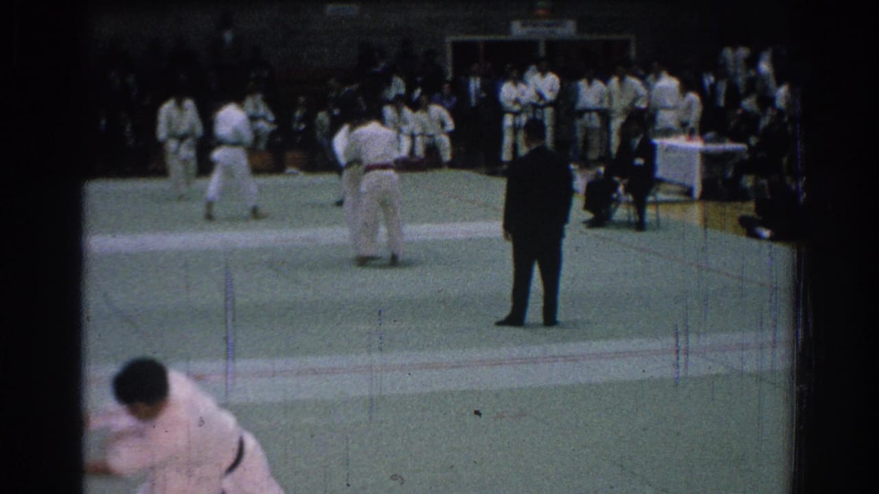 1966 San Gabriel footage shows martial arts students in white gi on a green mat, with a dark-suited referee and spectators in the background.