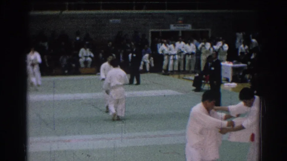 The 8mm frame shows a wider view of the mat, with competitors in white gi, a referee, and a nearer pair at the edge of the frame.
