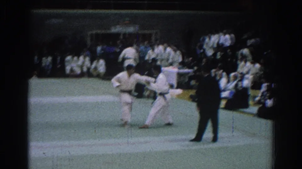 A 1966 San Gabriel karate match frame shows one competitor extending a leg while another stays in range near the referee and crowd.