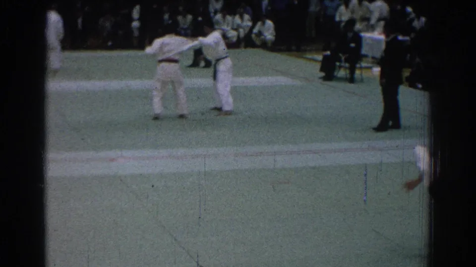 Two competitors in white gi reset or face each other on the green mat during the 1966 San Gabriel judo event.