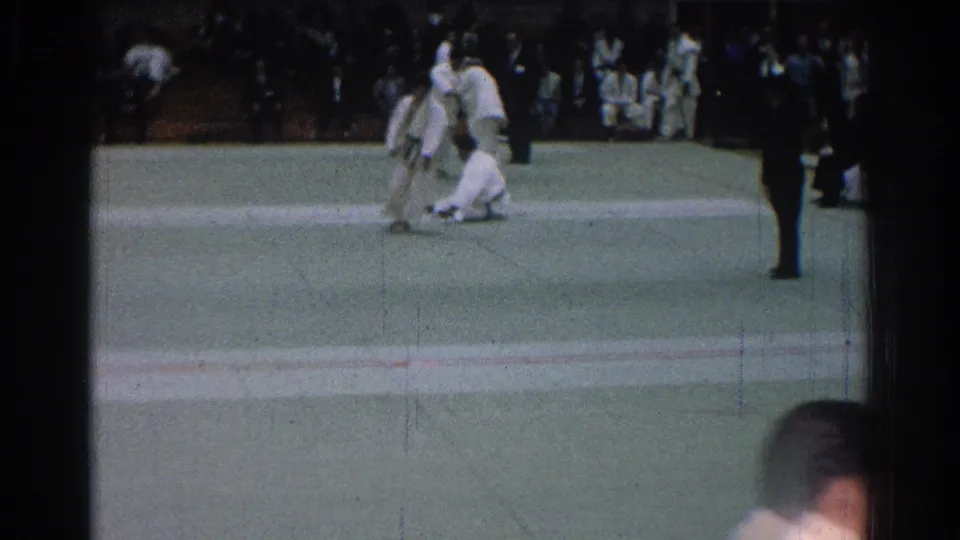 A judo competitor stands as another crouches or falls on the green mat during the 1966 indoor match in San Gabriel.
