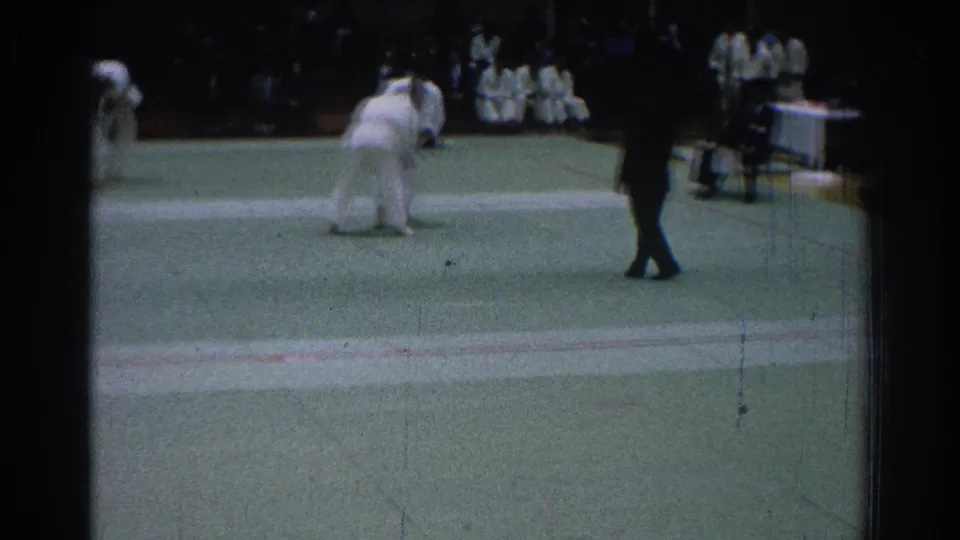 1966 San Gabriel judo tournament footage showing two competitors in white gi grappling on a green mat with a referee nearby.