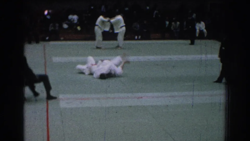 1966 San Gabriel indoor martial arts bout with competitors on the mat and officials watching from the side.