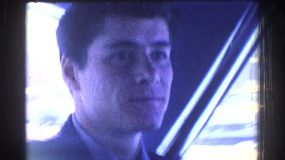 Close-up of an adult man's face under blue-tinted light, likely from the same 8mm home-movie reel after the judo scene.