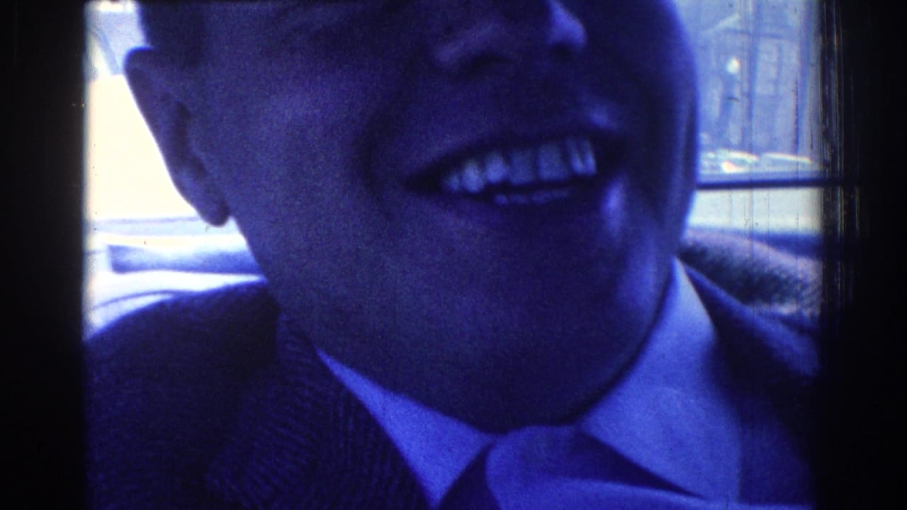 Close-up of a laughing man in a suit and tie inside a vehicle.