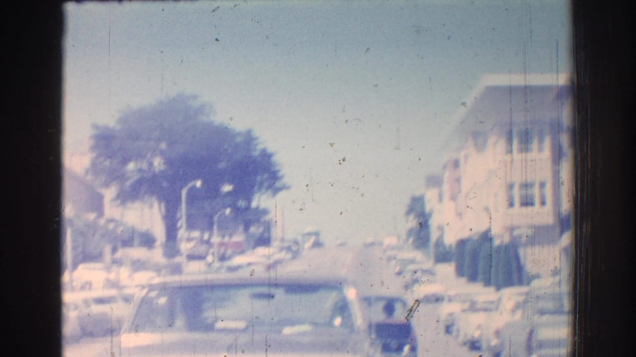 1966 San Gabriel street scene viewed through a car window, with parked cars, street trees, and low residential buildings.