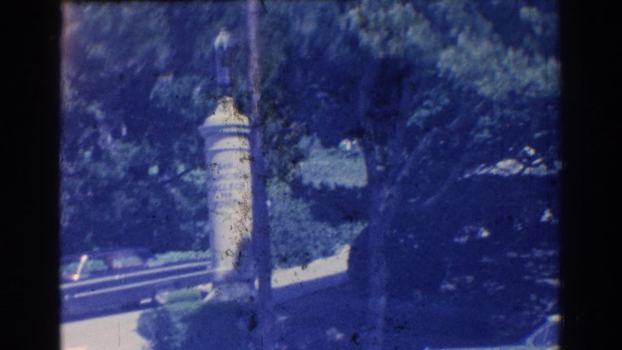 Stone monument or marker in a shaded park with trees and a road nearby.
