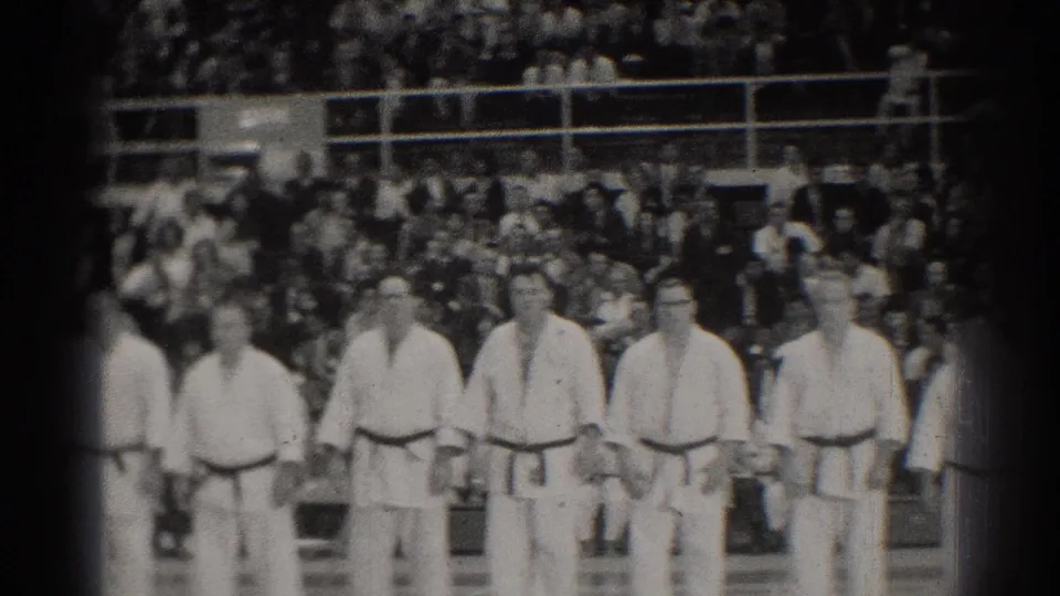 A closer 8mm view shows karate practitioners in white uniforms lined across a gymnasium with spectators behind them.