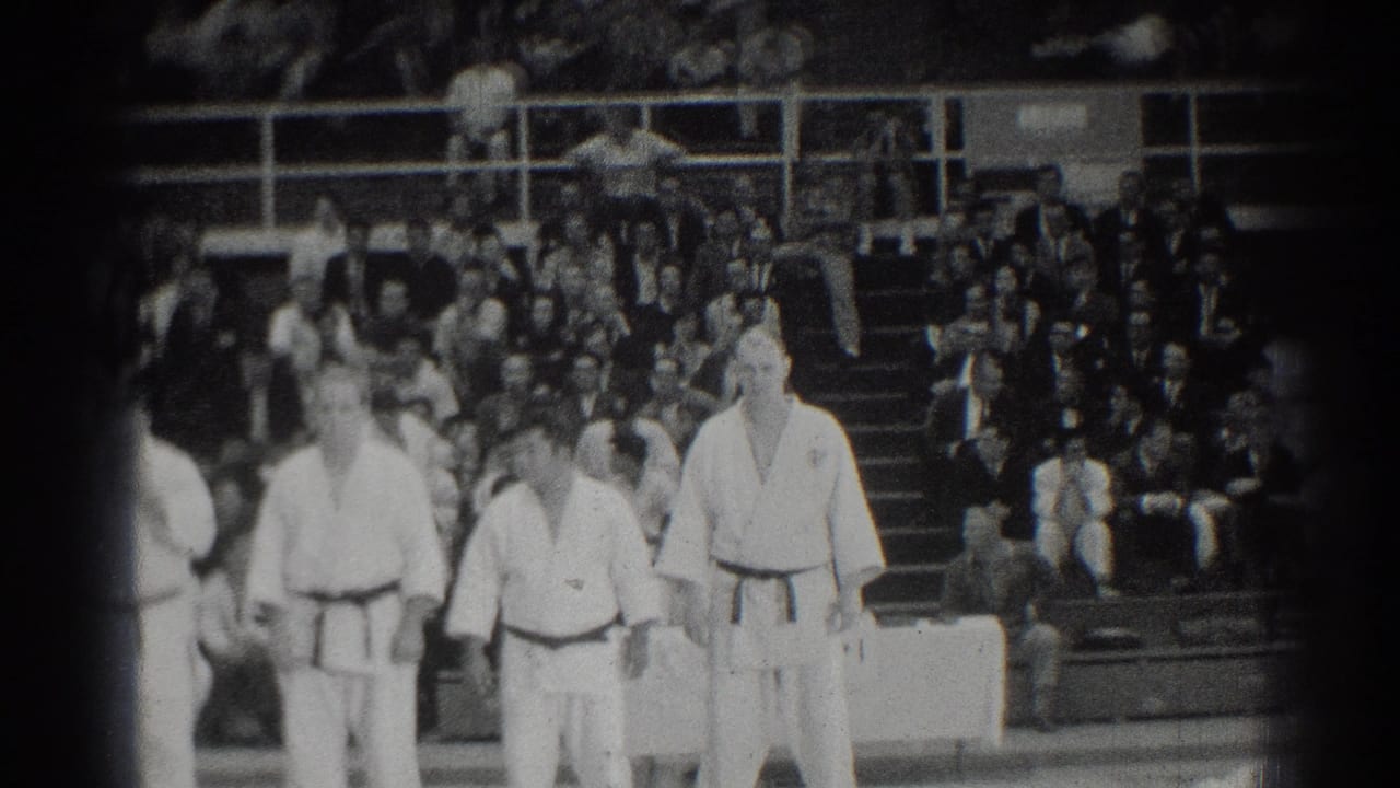 Judo athletes in white gi stand on a mat before crowded bleachers.