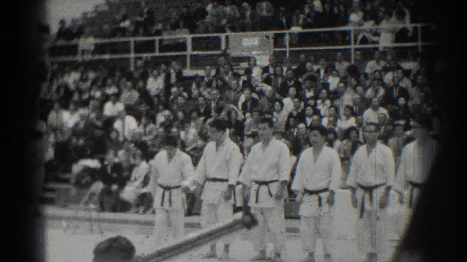 A closer spectator view shows judo athletes in formation at a 1966 San Gabriel, California meet, with the crowd and railings behind them.