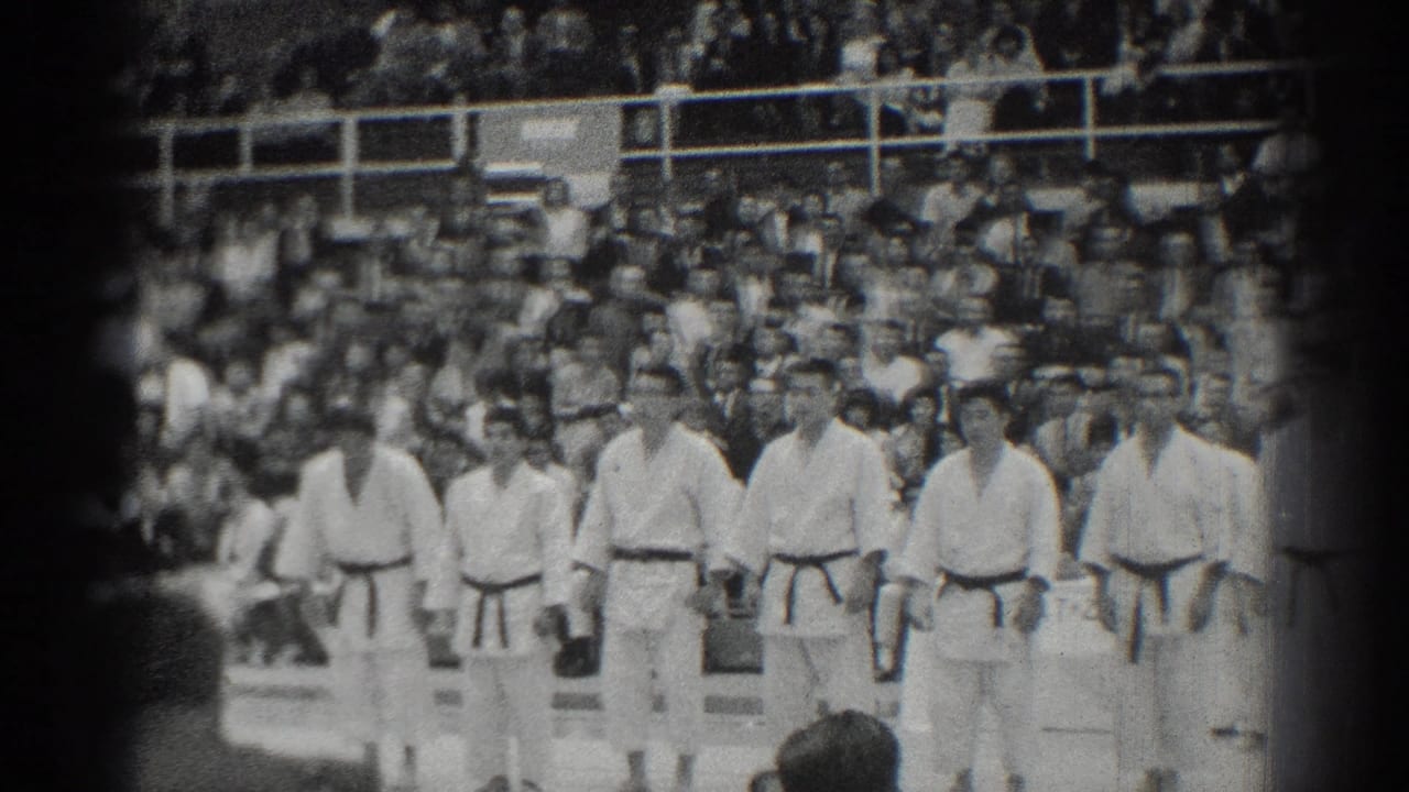 Martial artists stand at attention as spectators fill the bleachers behind them.