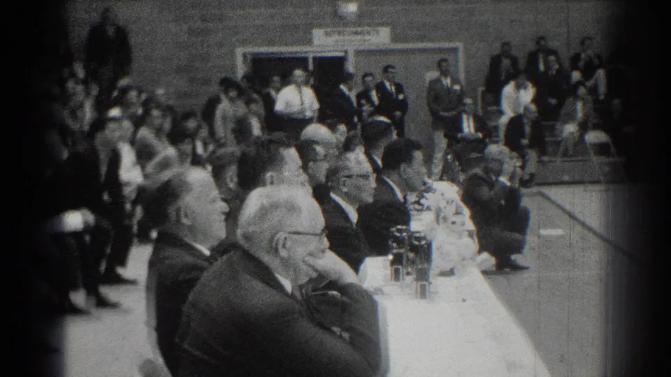 San Gabriel, California 1966 frame showing seated judges, bleachers, and spectators at an indoor karate event.