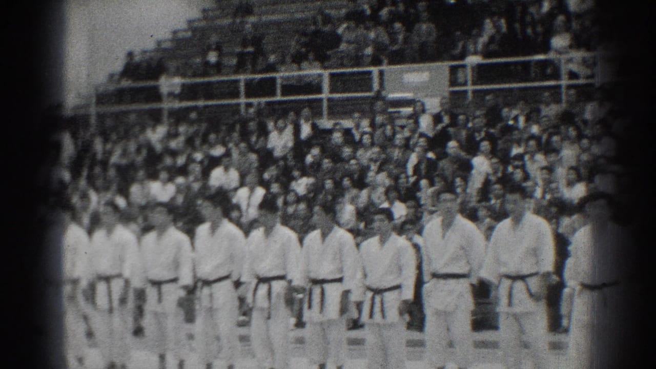 In San Gabriel, California, 1966, judo athletes in white gi and dark belts stand in a line as spectators fill the bleachers behind them.