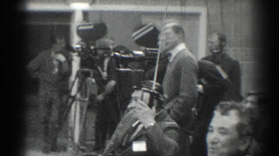 San Gabriel 1966 black-and-white frame with camera operators, tripods, and suited men at a press-style indoor gathering.
