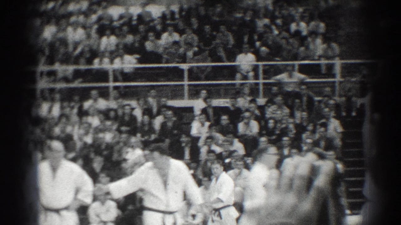 Martial arts participants in white uniforms stand before a crowded set of bleachers.