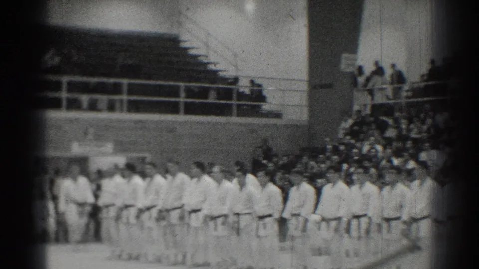 1966 San Gabriel gymnasium scene with martial artists standing in formation while spectators watch from bleachers.