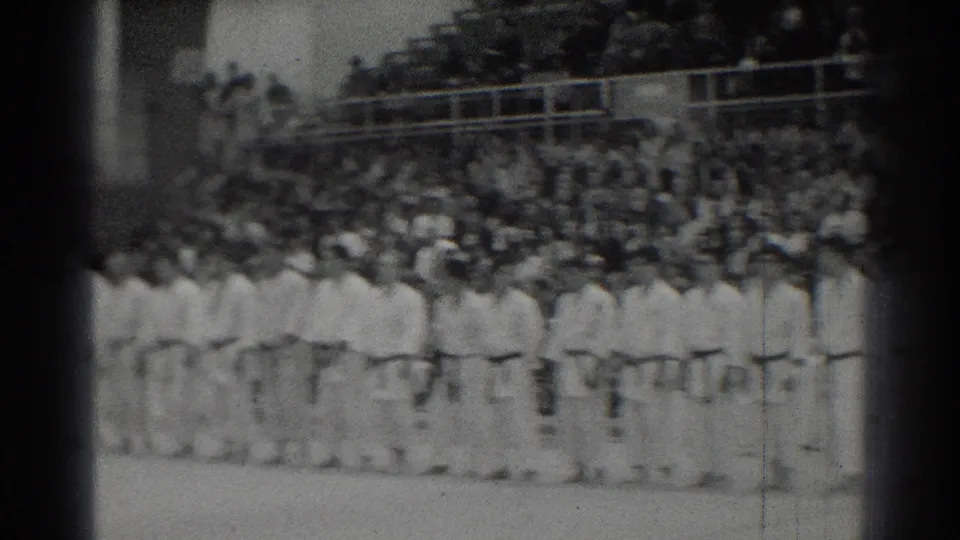 1966 San Gabriel martial arts competitors appear lined up in white gi while spectators fill bleachers behind them.